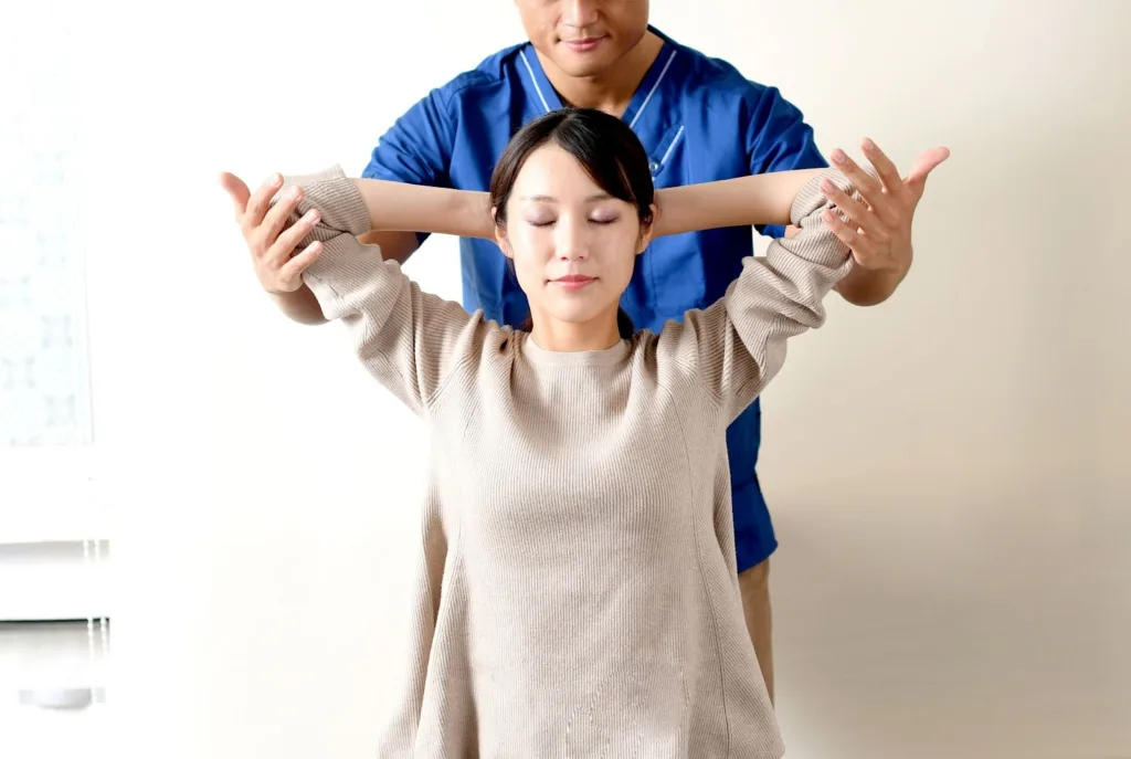 整体師に補助されながら肩のストレッチをする女性
