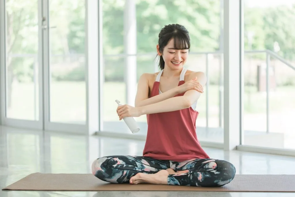 ヨガマットの上で日焼け止めを塗る女性