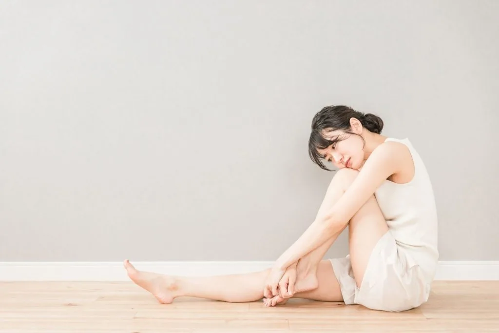 体育座りで左脚をさする女性
