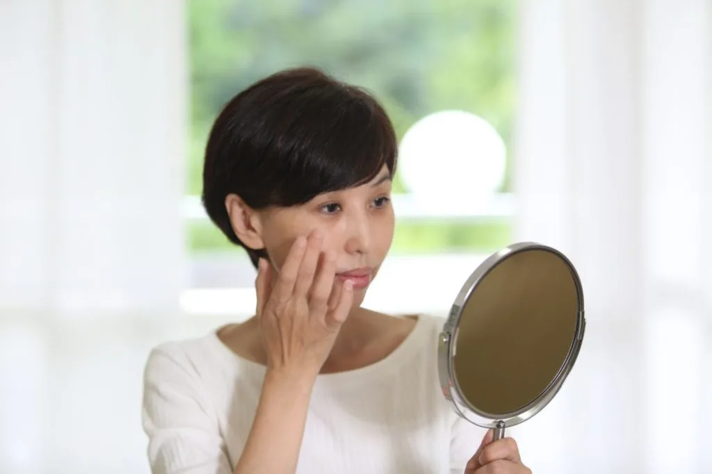 手鏡で顔の歪みをチェックする女性
