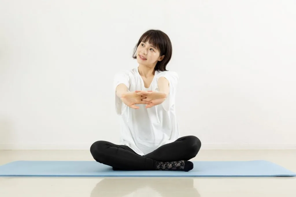 あぐらをかきながら腕を伸ばす女性