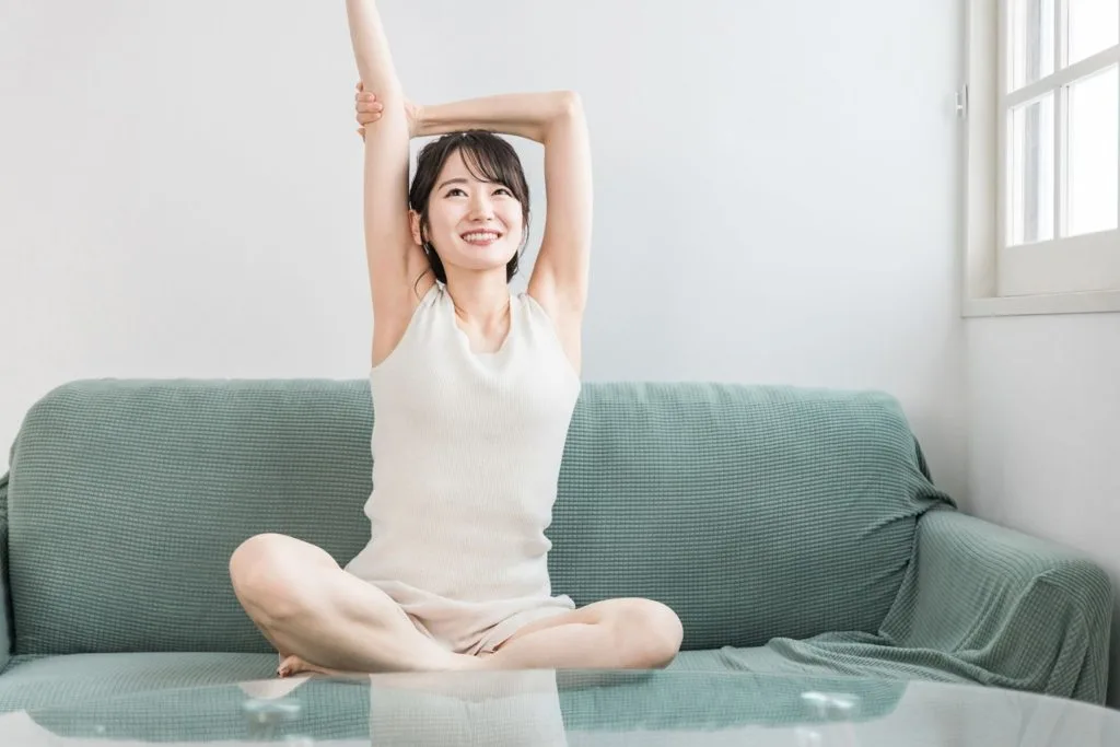 あぐらをかきながら肩のストレッチをする女性