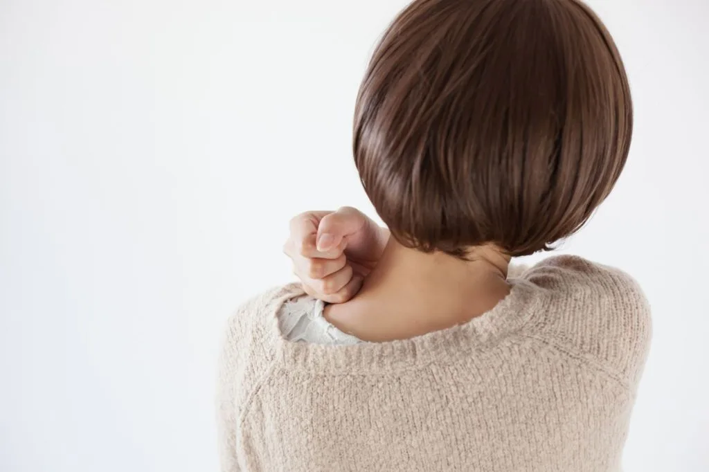 右手で左肩を叩く女性